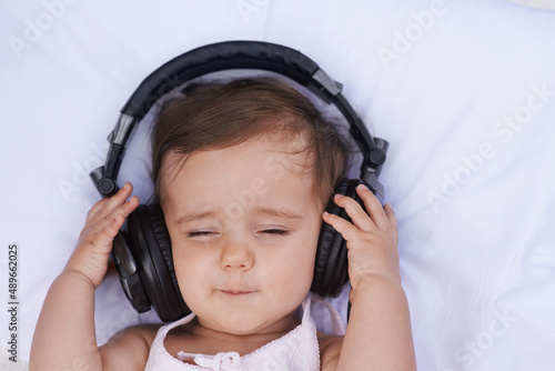 Listening to lullabies. A cute young baby girl listening to music on headphones.