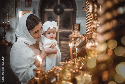 Fotografija a mother with a small child in a temple or church prays near an icon and candles