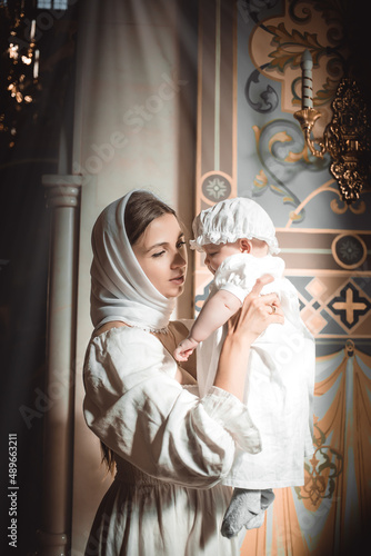 a mother with a small child in a temple or church prays near an icon and candles or came to a divine service in the Russian Orthodox church, the baptism of a baby