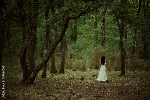 Woman wearing white dress walking into green forest