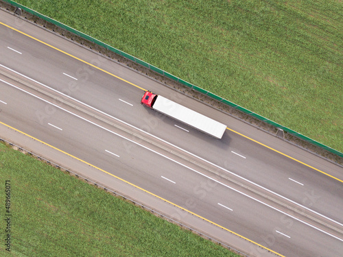 Dump trucks carrying goods on the highway. Red truck driving on asphalt road along the green fields. seen from the air. Aerial view landscape. drone photography. cargo delivery