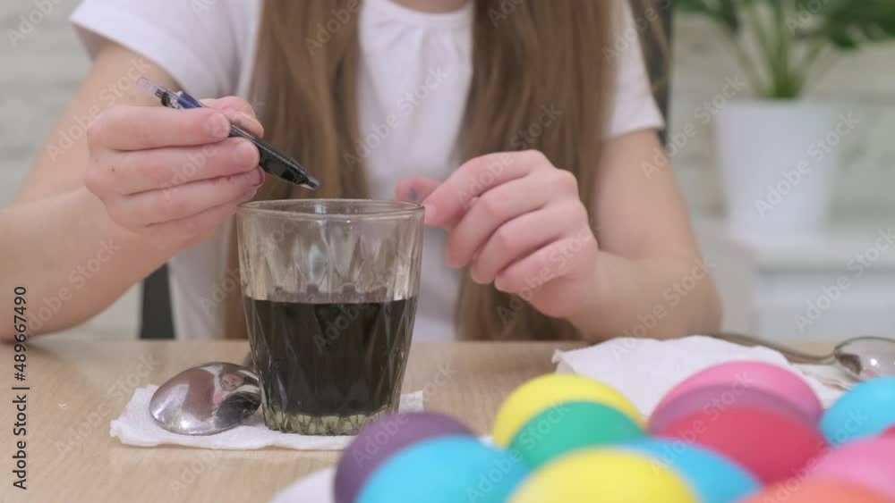 Little girl painting eggs with water food colors for easter. Multi-colored painted eggs lie in a plate on the table. Child preparing for holiday at home Little girl painting eggs with water food colors for easter. Multi-colored painted eggs lie in a plate on the table. Child preparing for holiday at home