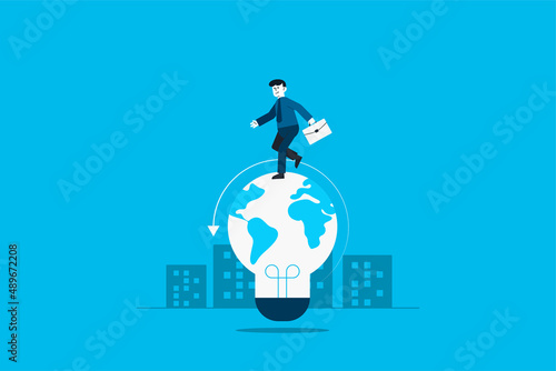 Businessman walks on lightbulb with world map.