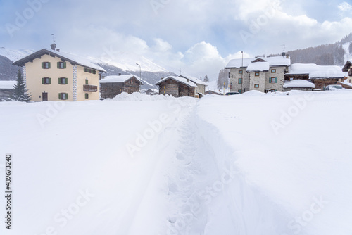 Footprints on pathway in snowdrifts leading towards homes in mountain village. The way forward or way home concept © hopsalka