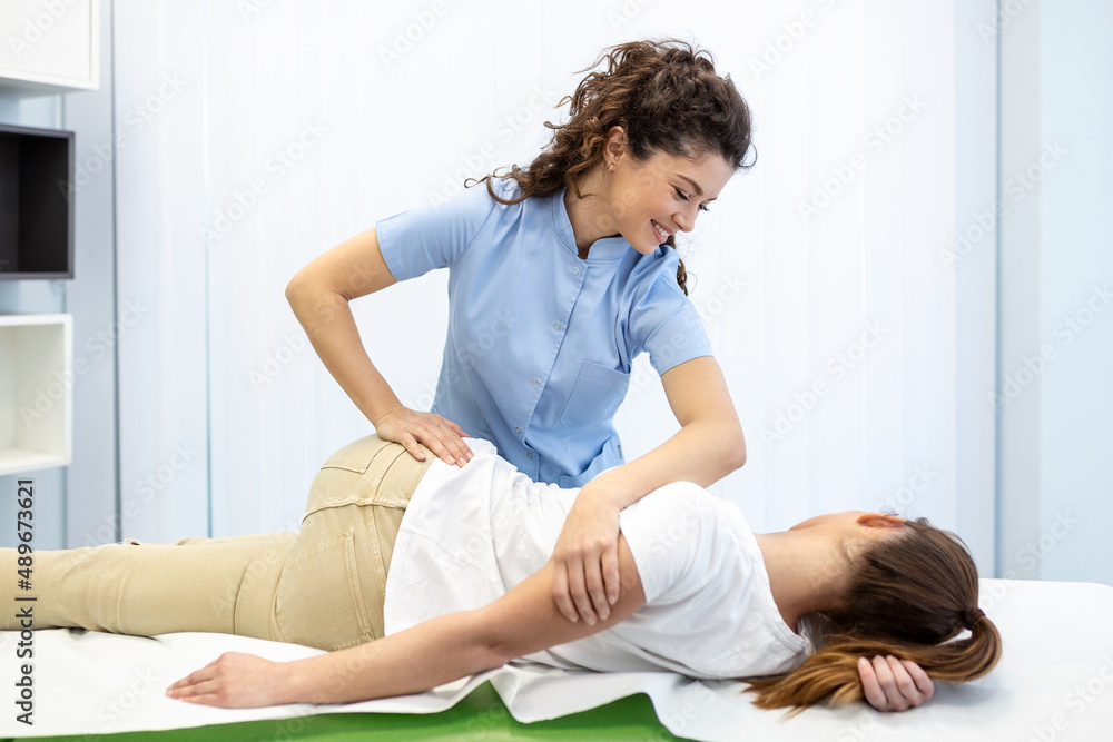 Young woman doctor chiropractor or osteopath fixing lying womans back with hands movements during visit in manual therapy clinic. Professional chiropractor during work Young woman doctor chiropractor or osteopath fixing lying womans back with hands movements during visit in manual therapy clinic. Professional chiropractor during work