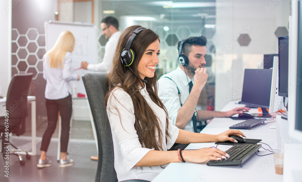 Young positive woman customer support phone operator in microphone headset working on computer in the office Young positive woman customer support phone operator in microphone headset working on computer in the office