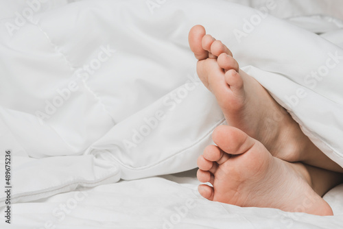 Childs legs are covered with white bed linen. The warmth of home comfort.