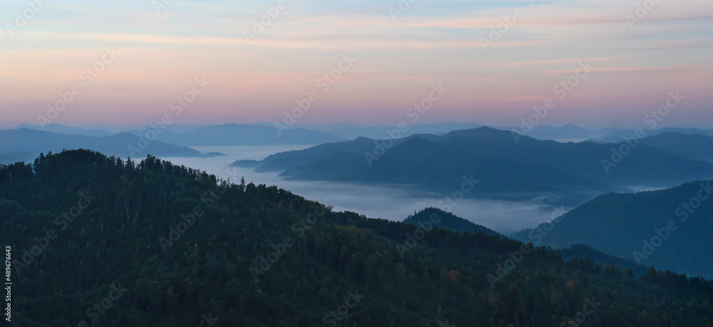 Fantastic dawn in the mountains. The horizon is red. The mountains are covered with forests. Fog in the valleys