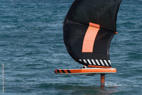 A man is wing foiling using handheld inflatable wings and hydrofoil surfboards in a blue ocean, rider on a wind wing board, surf the waves photo