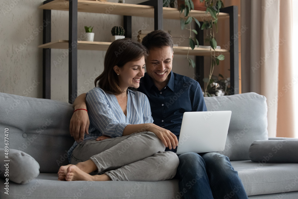 Happy loving millennial married family couple looking at laptop screen, watching funny comedian film, shopping in internet store or planning trip vacation, modern technology addiction concept. Happy loving millennial married family couple looking at laptop screen, watching funny comedian film, shopping in internet store or planning trip vacation, modern technology addiction concept.