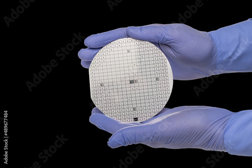 A hands in a rubber glove hold a multilayer semiconductor silicon wafer with a microcircuit chip of a powerful Darlington transistor isolated on a black background