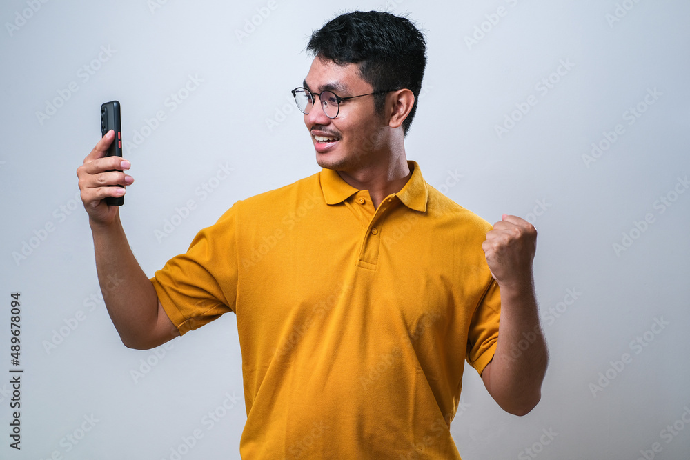 Adult Asian man showing happy gesture while looking to his mobile phone Adult Asian man showing happy gesture while looking to his mobile phone