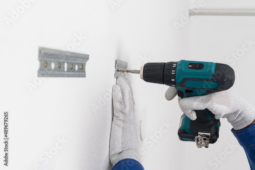 Fotografie the hands of a worker, against the background of a white wall, fasten a bracket