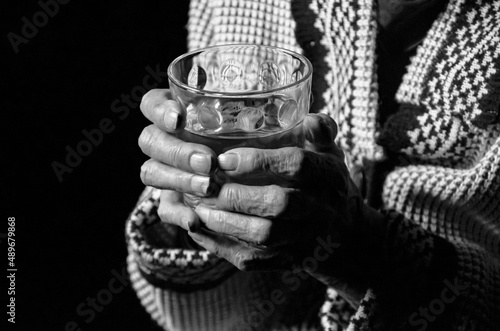Portrait of an elderly woman with a glass of water on a black background. Black and white photo.