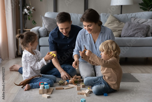 Affectionate millennial couple parents playing toys with adorable children son daughter  having fun enjoying playtime activity sitting together on floor carpet in living room  family relations concept
