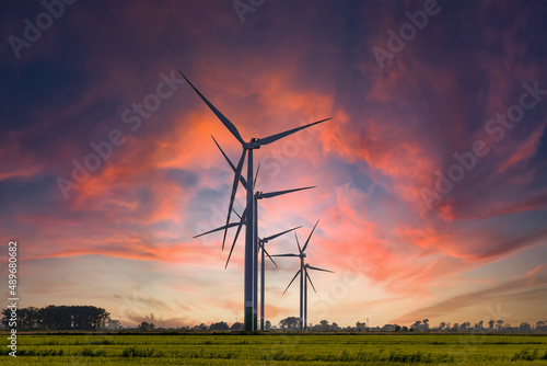 Fotografie Windmill farm on green meadow under moody red sky, green energy production using