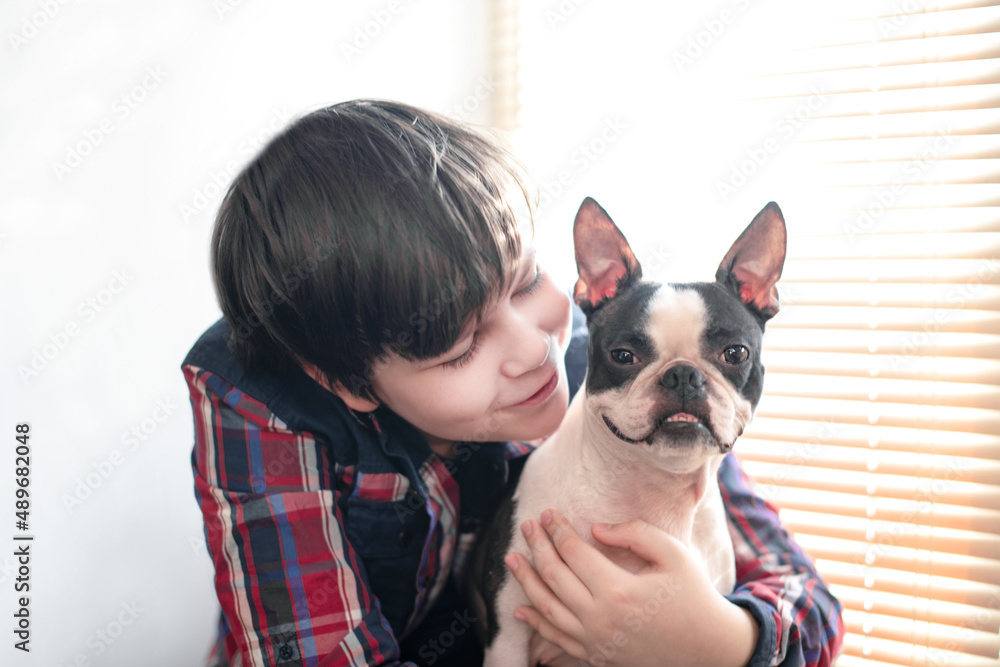 Boy lovingly hugging his happy friend boston terrier dog with a smile on his face at home. Pet care. Boy lovingly hugging his happy friend boston terrier dog with a smile on his face at home. Pet care.