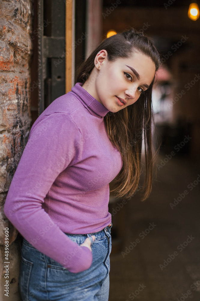 Photo of a brown-haired girl in a lilac Golf and jeans on the street in the city