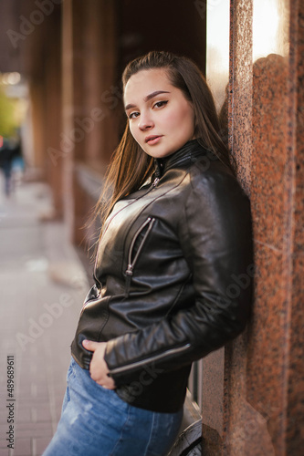 Photo of a brown-haired girl in a leather jacket and jeans on the street in the city