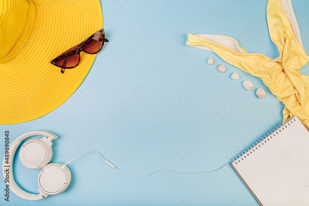 Beach flatlay, on a blue background swimming accessories, headphones and notepad, copyspace