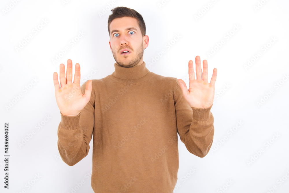 young caucasian man wearing grey turtleneck over white background afraid and terrified with fear expression stop gesture with hands, shouting in shock. Panic concept. young caucasian man wearing grey turtleneck over white background afraid and terrified with fear expression stop gesture with hands, shouting in shock. Panic concept.