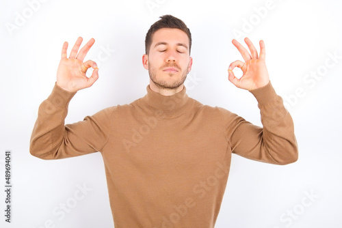 young caucasian man wearing grey turtleneck over white background relax and smiling with eyes closed doing meditation gesture with fingers. Yoga concept.