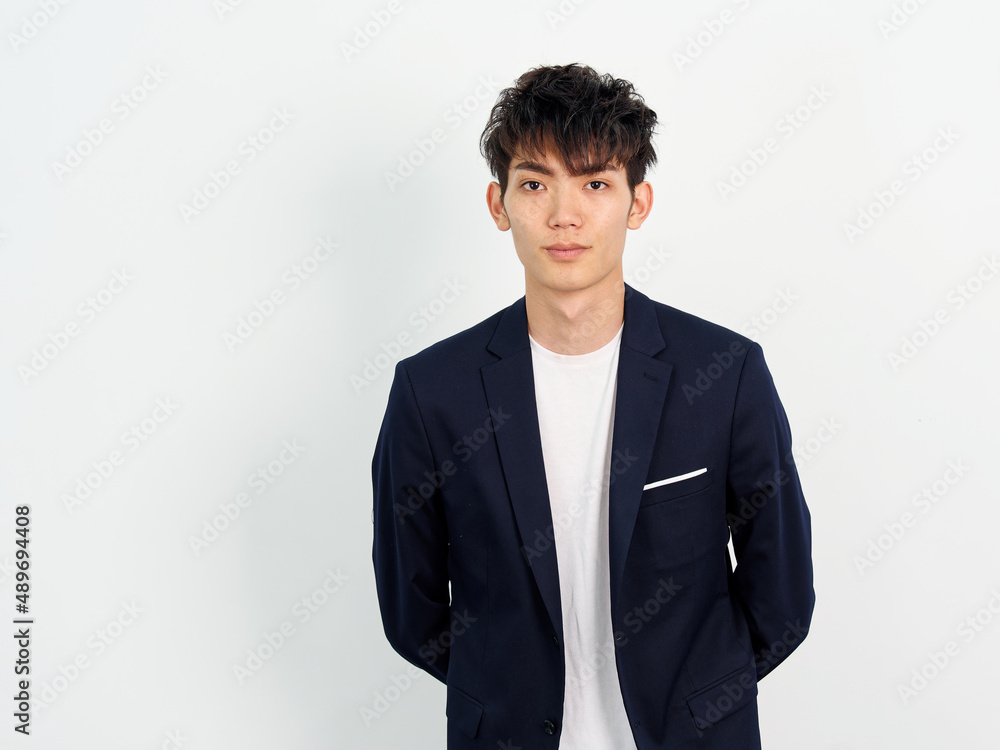 Portrait of handsome Chinese young man in dark blue leisure suit posing against white wall background. Arms on back and looking at camera, looks confident, front view. Portrait of handsome Chinese young man in dark blue leisure suit posing against white wall background. Arms on back and looking at camera, looks confident, front view.