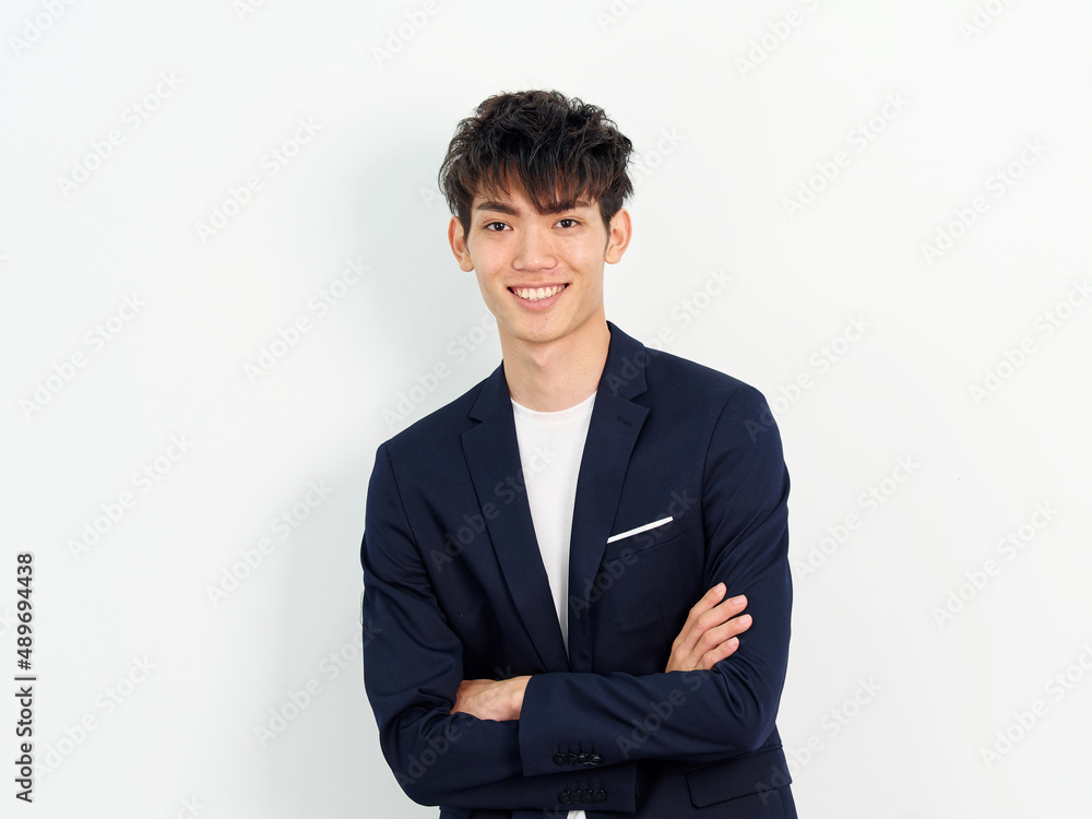 Portrait of handsome Chinese young man in dark blue leisure suit posing against white wall background. Arms crossed with mobile phone in hand and looking at camera, looks confident, front view Portrait of handsome Chinese young man in dark blue leisure suit posing against white wall background. Arms crossed with mobile phone in hand and looking at camera, looks confident, front view