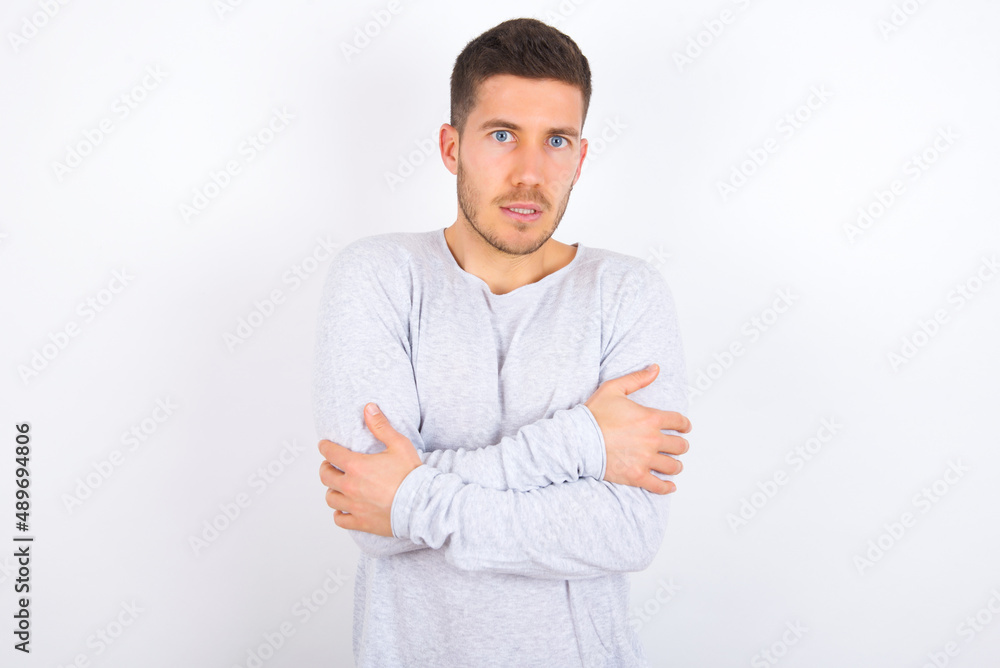young caucasian man wearing grey sweater over white background shaking and freezing for winter cold with sad and shock expression on face. young caucasian man wearing grey sweater over white background shaking and freezing for winter cold with sad and shock expression on face.