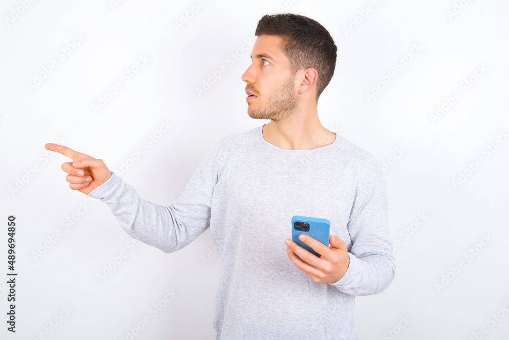 Stunned young caucasian man wearing grey sweater over white background points sideways right copy space, recommends product, sees astonishing thing Stunned young caucasian man wearing grey sweater over white background points sideways right copy space, recommends product, sees astonishing thing