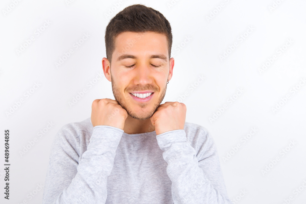 young caucasian man wearing grey sweater over white background grins joyfully, imagines something pleasant, copy space. Pleasant emotions concept. young caucasian man wearing grey sweater over white background grins joyfully, imagines something pleasant, copy space. Pleasant emotions concept.