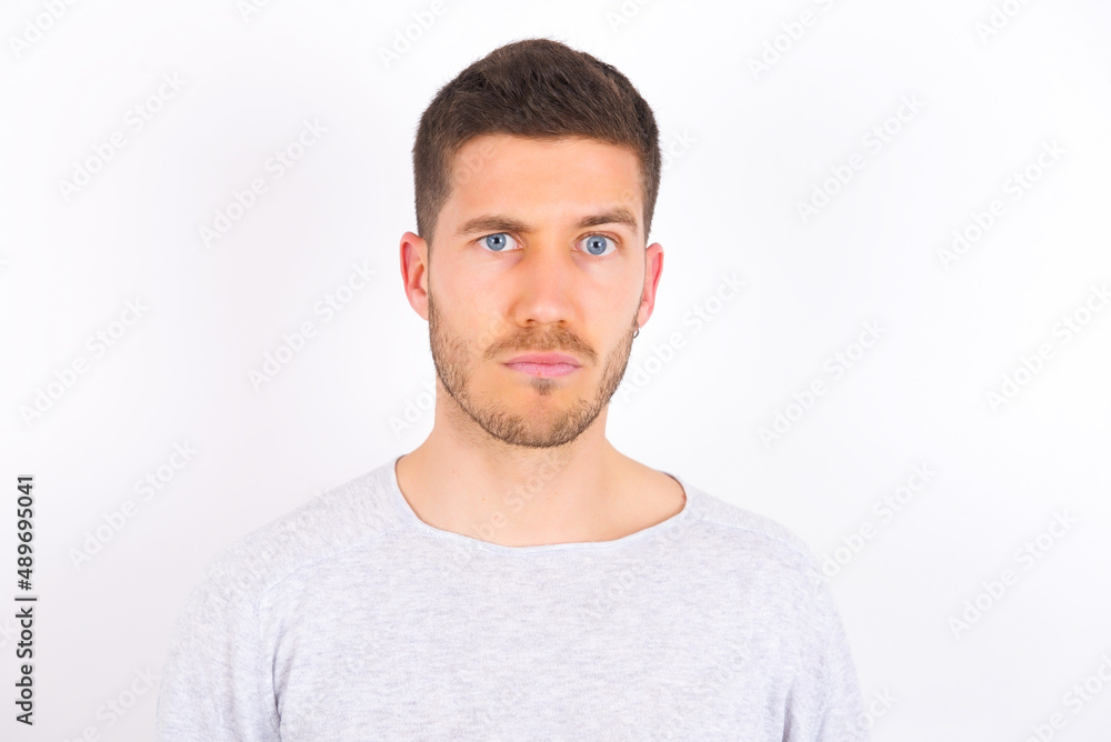 Fototapeta premium Displeased young caucasian man wearing grey sweater over white background frowns face feels unhappy has some problems. Negative emotions and feelings concept