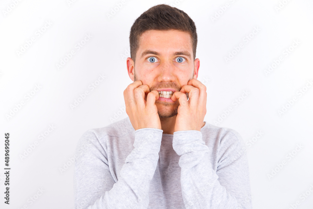 Terrified young caucasian man wearing grey sweater over white background looks empty space home alone moonless night Terrified young caucasian man wearing grey sweater over white background looks empty space home alone moonless night