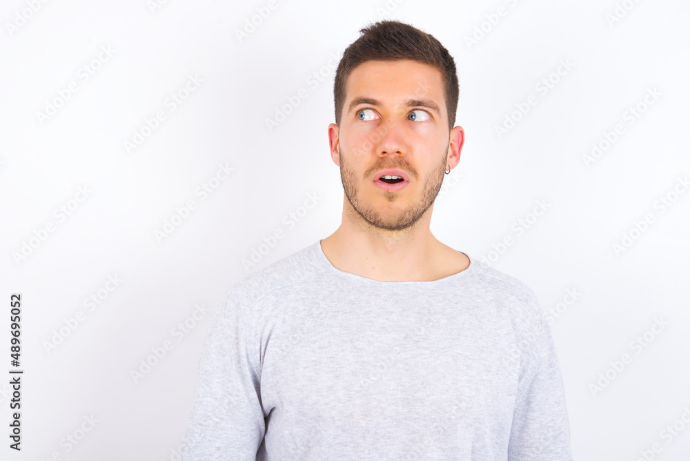 Obraz premium Shocked young caucasian man wearing grey sweater over white background look empty space with open mouth screaming: Oh My God! I can't believe this.