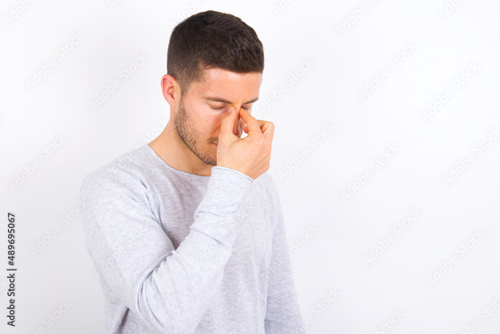 Sad young caucasian man wearing grey sweater over white background suffering from headache holding hand on her face Sad young caucasian man wearing grey sweater over white background suffering from headache holding hand on her face
