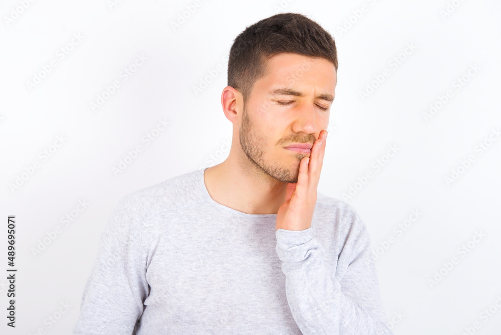 young caucasian man wearing grey sweater over white background with toothache young caucasian man wearing grey sweater over white background with toothache