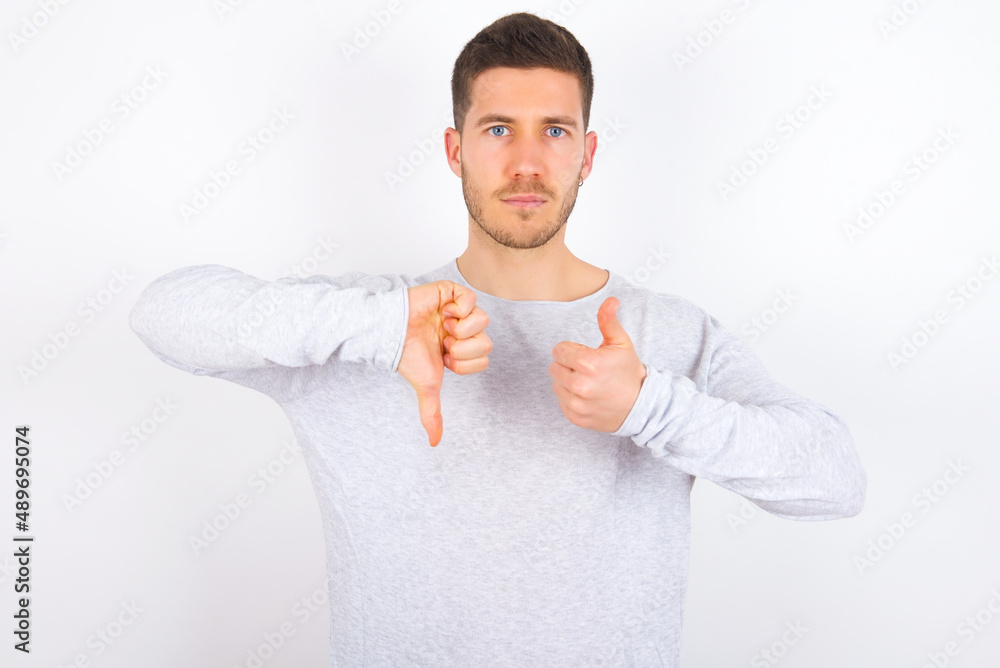 young caucasian man wearing grey sweater over white background showing thumb up down sign young caucasian man wearing grey sweater over white background showing thumb up down sign