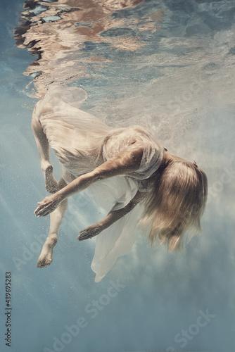 A woman in a dress swims underwater as if floating in zero gravity