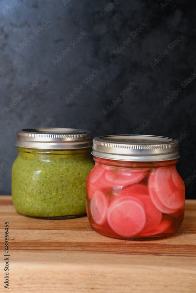 Jar of pesto and pickled radishes in front of a rustic background Jar of pesto and pickled radishes in front of a rustic background