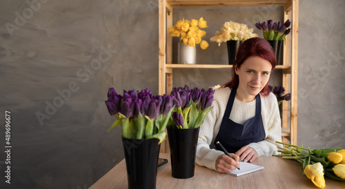 European flower shop concept. A woman florist is sitting at a table holding a pen in her hands and making requests for the delivery of plants and flowers to a flower shop.