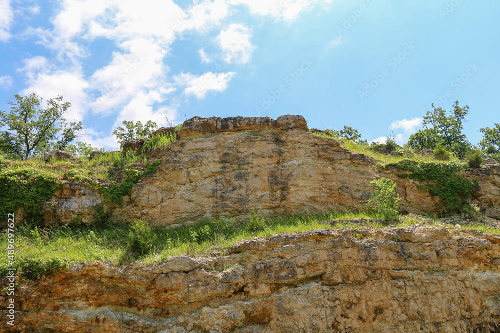 rocky stone cliff clouds blue sky daytime afternoon hill trees hillside tall foliage rural cliffs