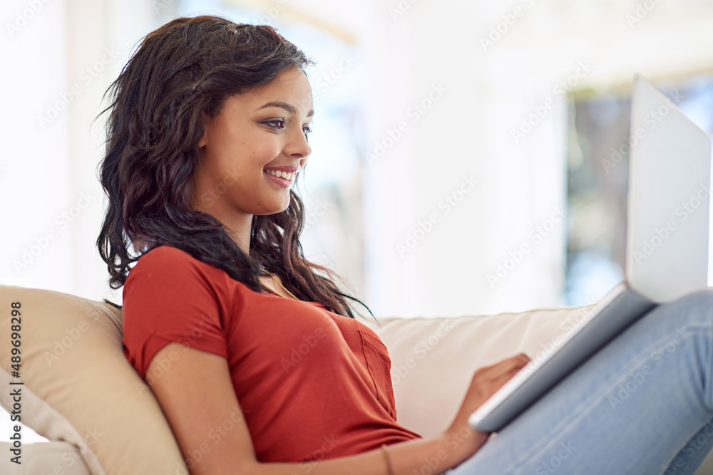 Catching up with whats happening online. Cropped shot of a young woman using her laptop while relaxing at home. Catching up with whats happening online. Cropped shot of a young woman using her laptop while relaxing at home.