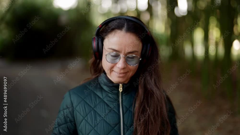 charming middle-aged woman is enjoying music by headphones, walking in park charming middle-aged woman is enjoying music by headphones, walking in park