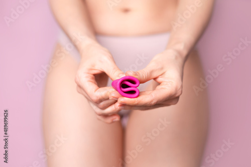A young woman folding a pink menstrual cup in her hand. Pink colored background. Space for text. Eco-friendly silicone women's health cycle