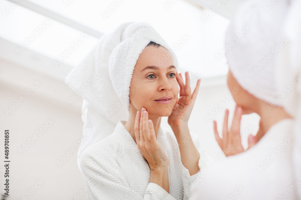 portrait of gorgeous happy middle age woman looking at mirror touching her skin