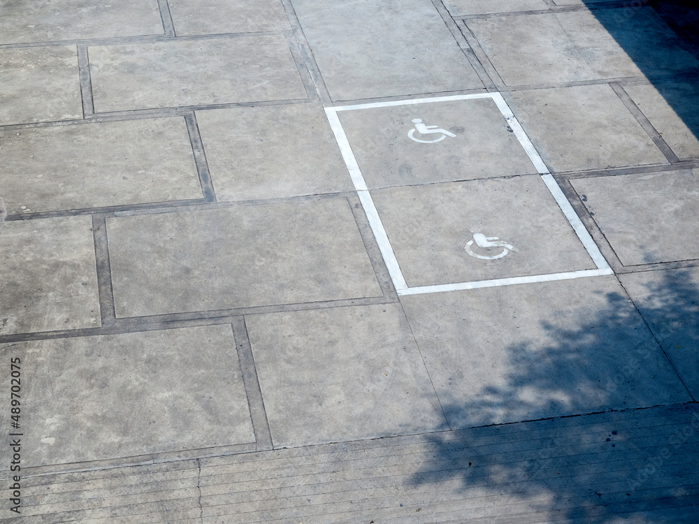 The old white handicapped icon symbol on the ground shows a sign reserved for disabled persons in a car parking space, top view.
