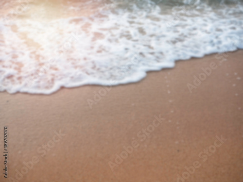 Blurred white splashing sea wave on sand beach with copy space. Blurry summer sunset beach background.