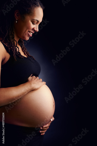 My baby is growing. A side profile of a tranquil pregnant woman holding her bare belly and looking down. photo