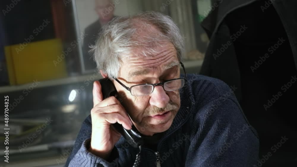 An elderly man with a mustache in glasses is talking on a landline phone and giving instructions. Elderly engineer calling on the phone An elderly man with a mustache in glasses is talking on a landline phone and giving instructions. Elderly engineer calling on the phone