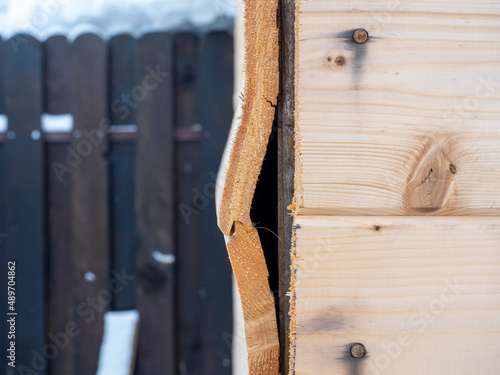 A close-up of a part of a wooden wall made of clapboard of poor quality. A hole in the wall, a curved board. The concept of low-quality construction and repair